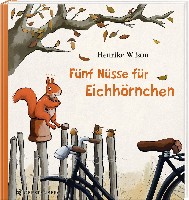 Ein Eichhörnchen sitzt auf einem Zaun und hat verschiedene Nüsse vor sich