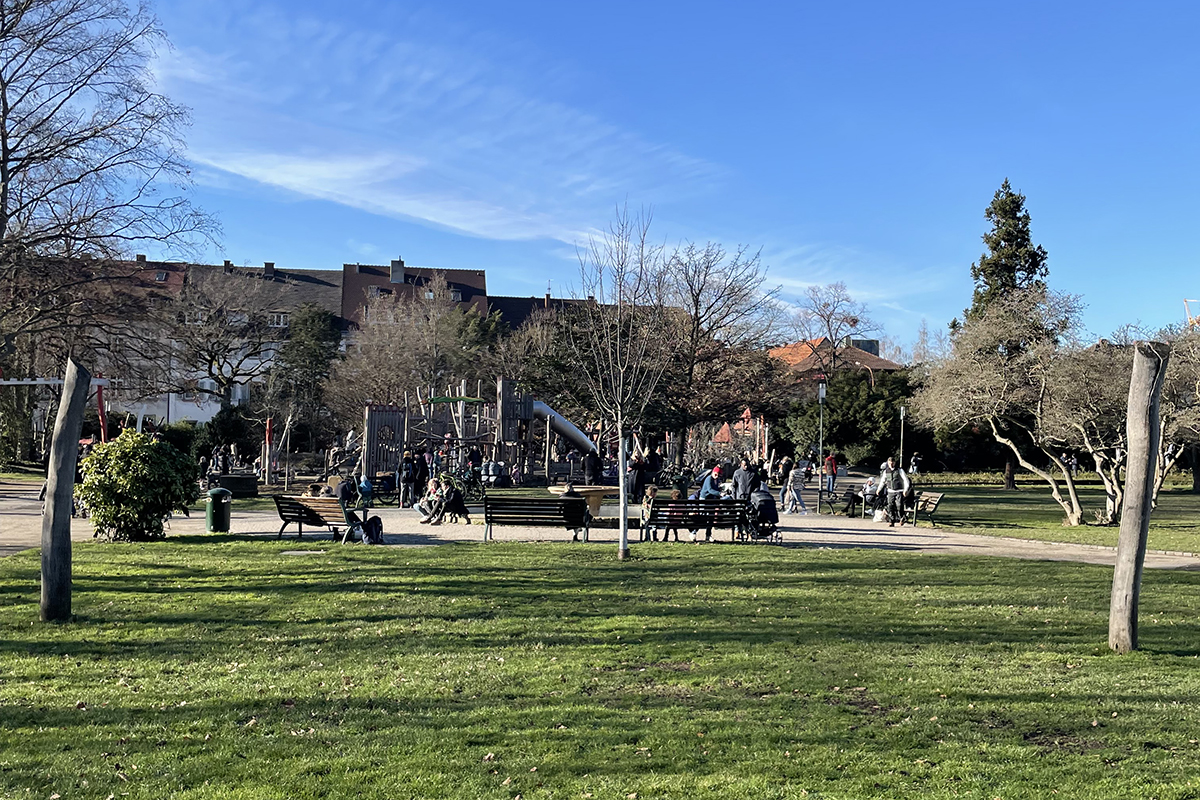 Zahlreich besuchter Spielplatz im Hintergrund; im Vordergrund grüne Wiese