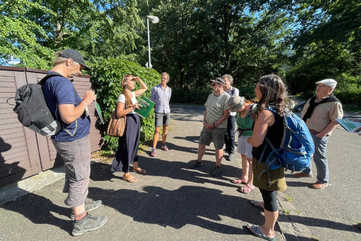 Begrünungsspaziergang An einem Straßeneck vor einer Mauer mit Fassadenbegrünung Verena Hilgers und um sie rum Zuhörende
