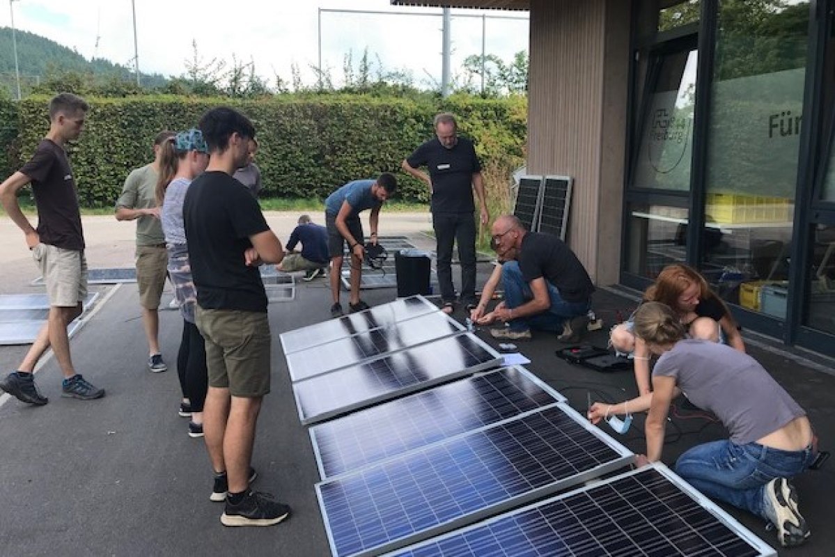 Balkonsolar Auf dem Boden Solarmodule drumherum Menschen, die daran basteln.