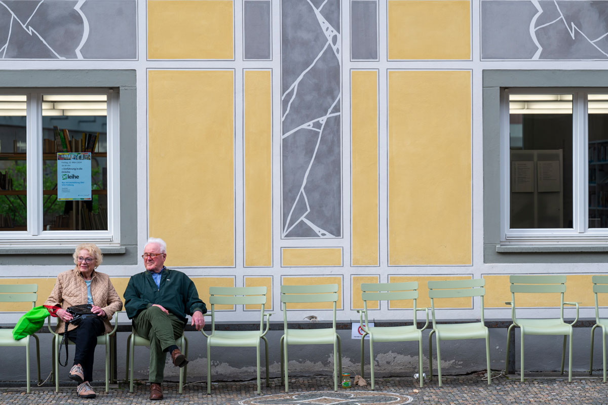 Frau und Mann sitzen auf grünen Stühlen vor der Stadtbibliothek