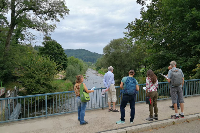 fünf Personen Stehen am Geländer der Sandfangbrücke und schauen auf die Dreisam.