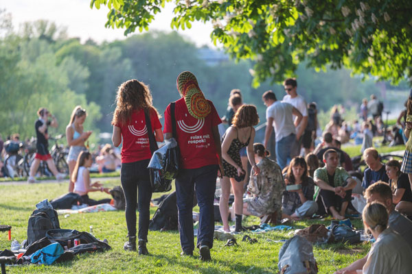 Zwei Nachtmediator*innen gehen durch einen Park mit vielen jungen Menschen